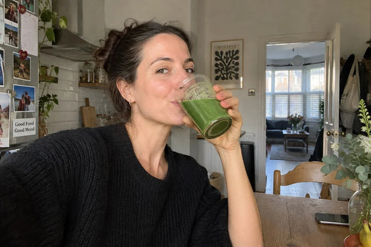 Woman drinking a green smoothie in a sunlit home kitchen.